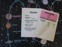 Close-up image of the Solarquest game board showing Pluto as a pinkish planet and Charon as its orange-coloured satellite. Also shown are title deed cards for Pluto and Charon in the game